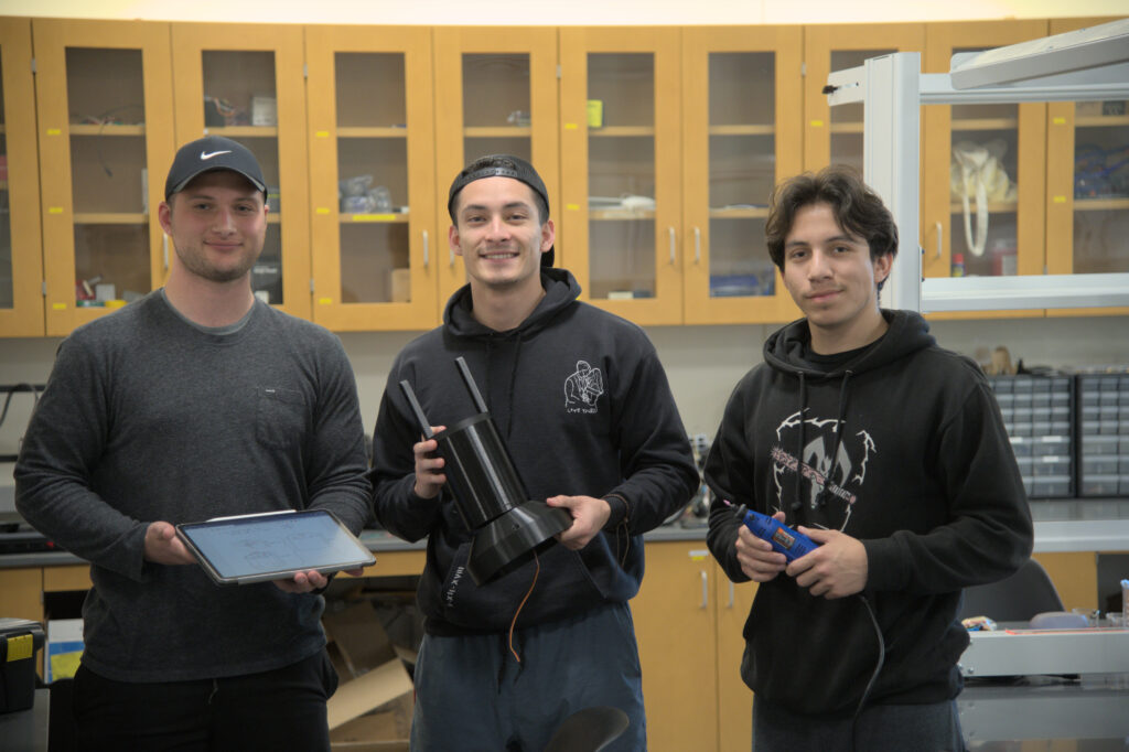 Sam Bettencourt, Angel Martinez, and Sebastian Guerrero Mejia pose with their Capstone projects in robotics.